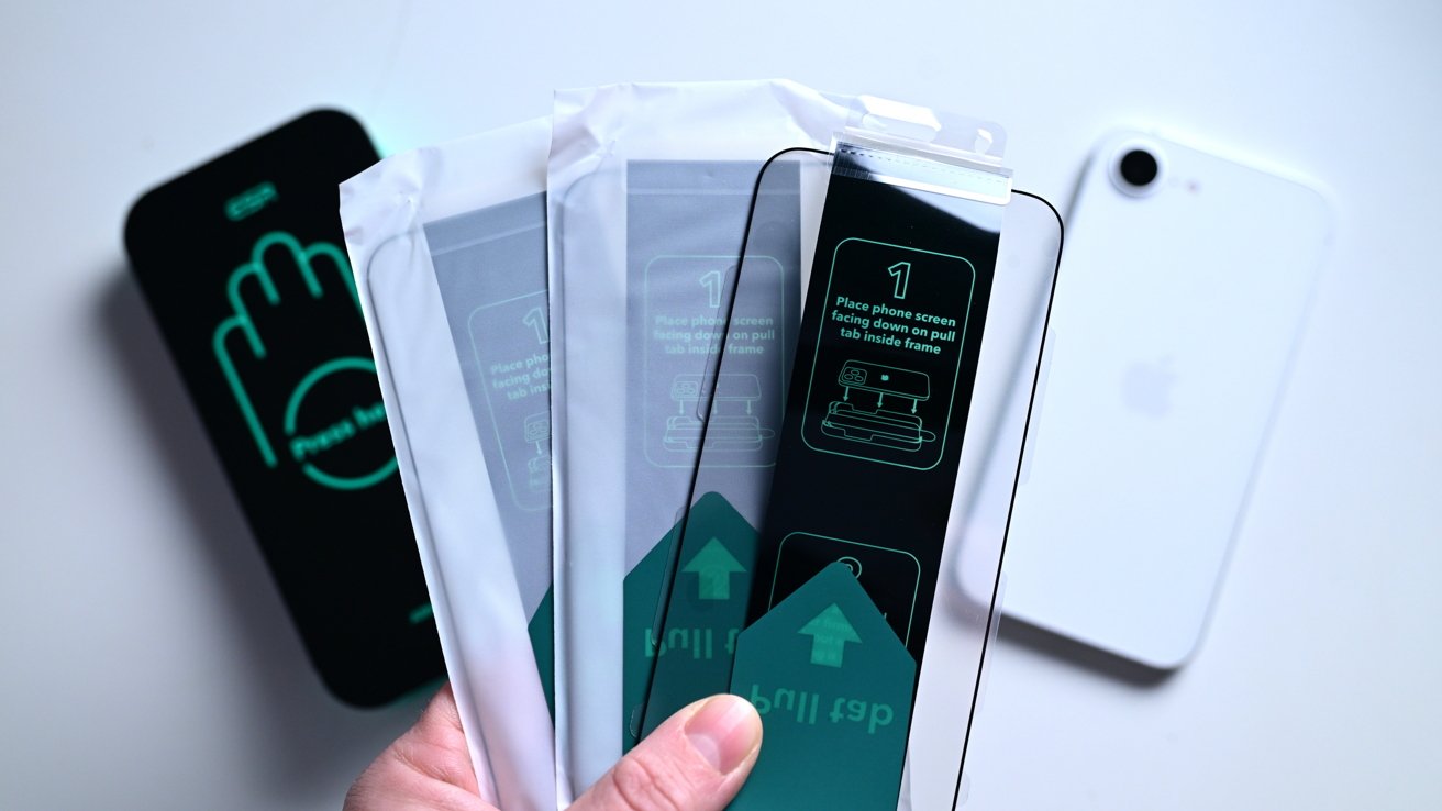 Hand holding three smartphone screen protectors beside a white smartphone, with installation instructions visible on the packaging.