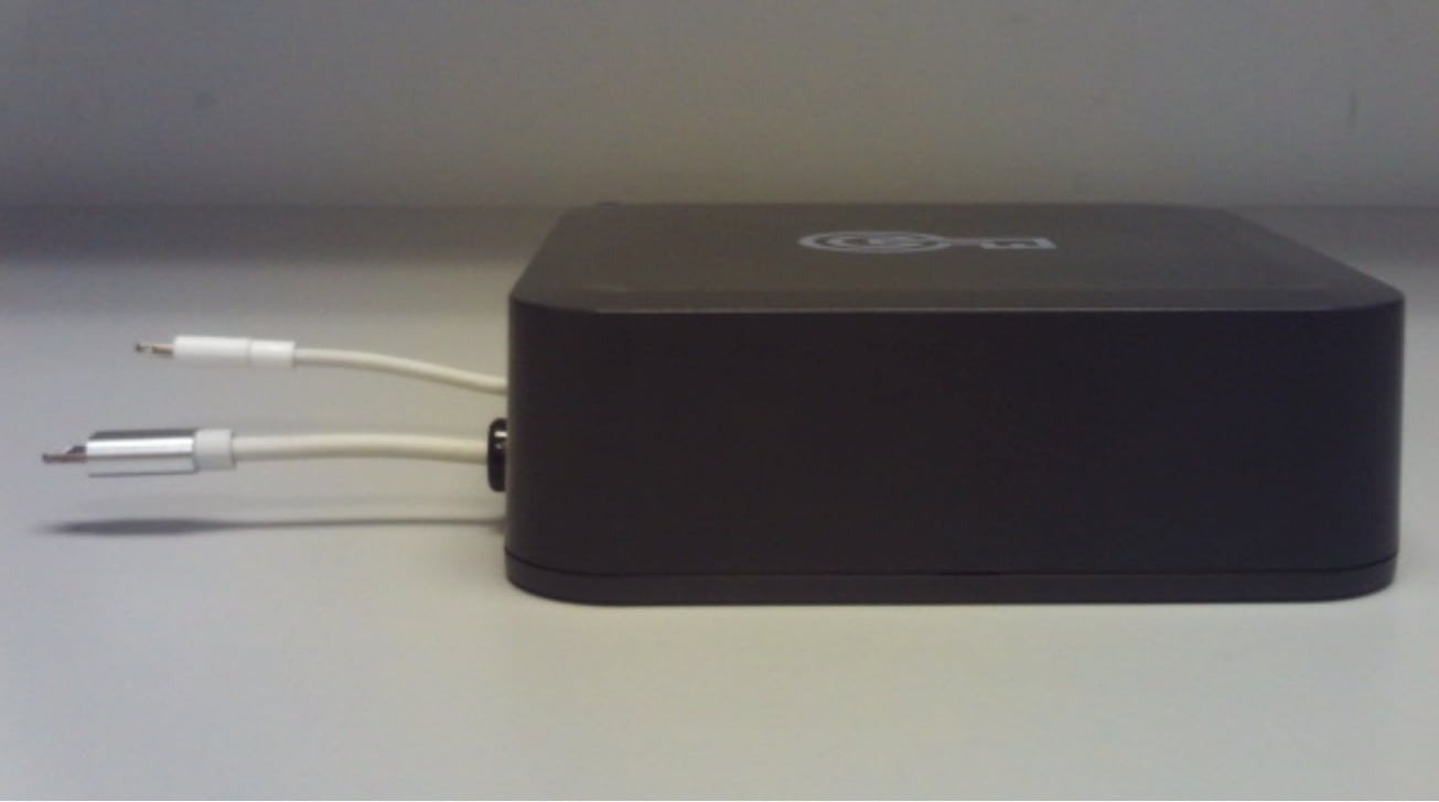 A black rectangular device with two white cables extending from its side, placed on a light-colored surface.