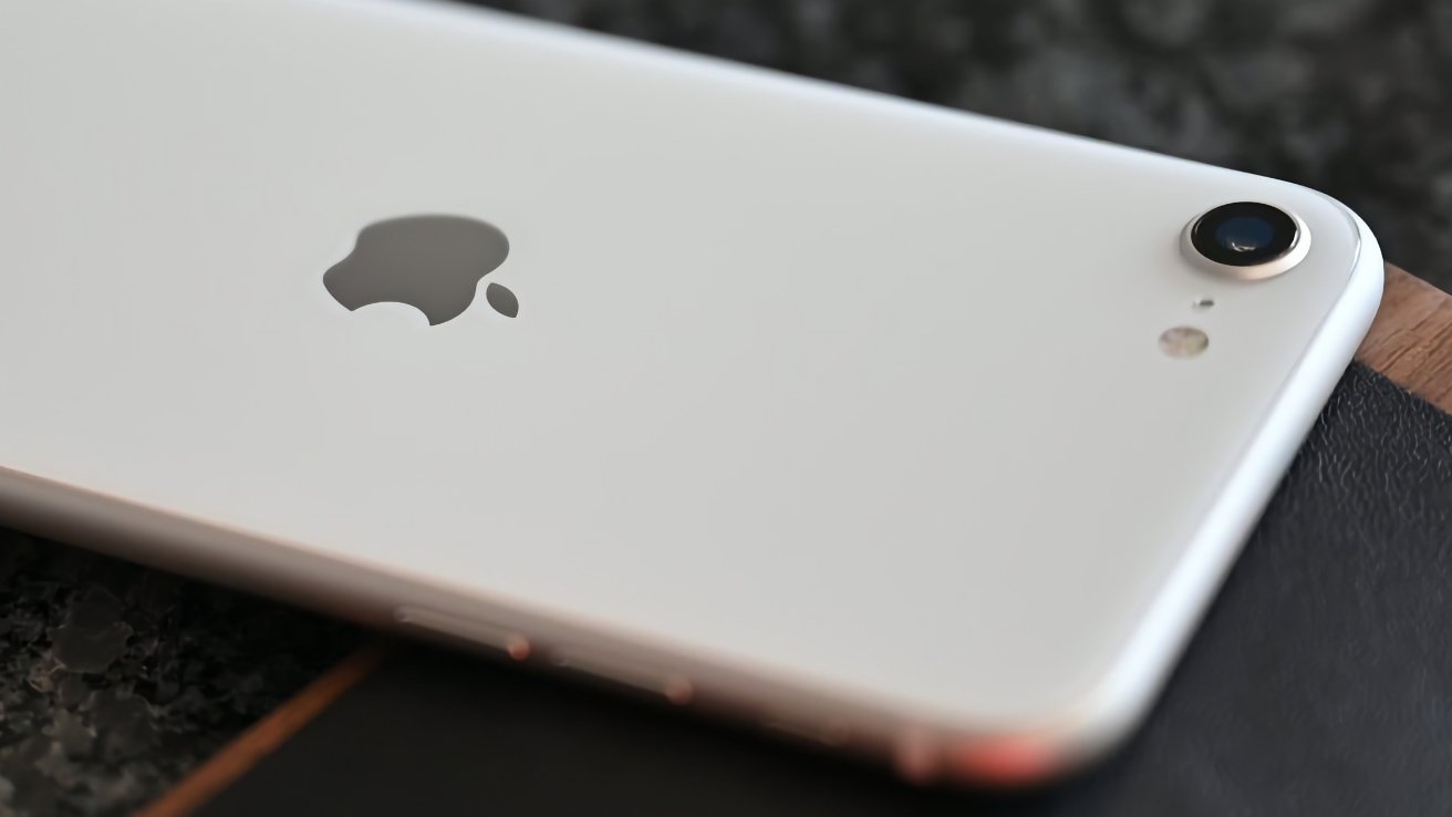 Close-up smartphone putih dengan logo Apple perak dan kamera belakang tunggal di permukaan gelap.