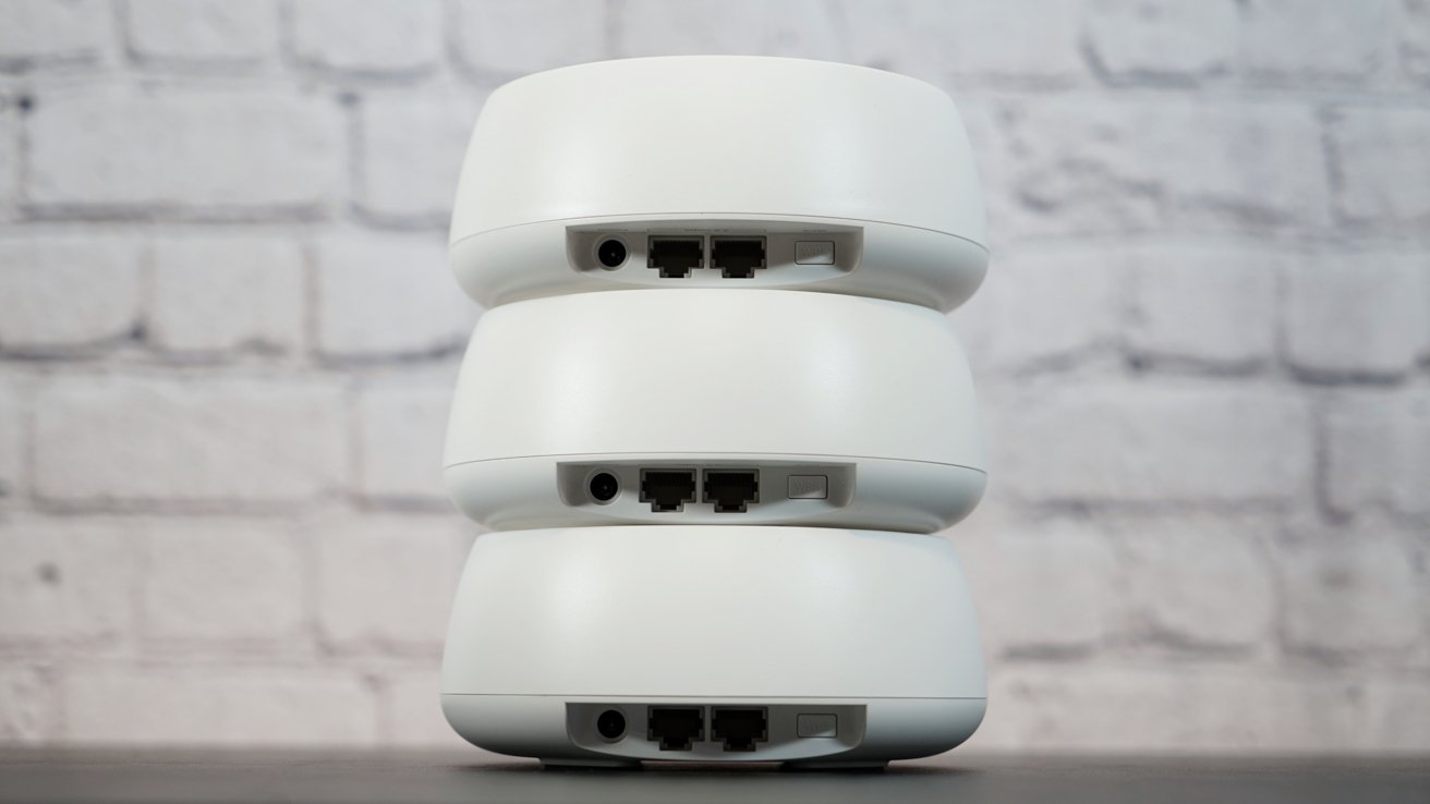 Three stacked white round Wi-Fi routers with visible ports, against a white brick wall background.