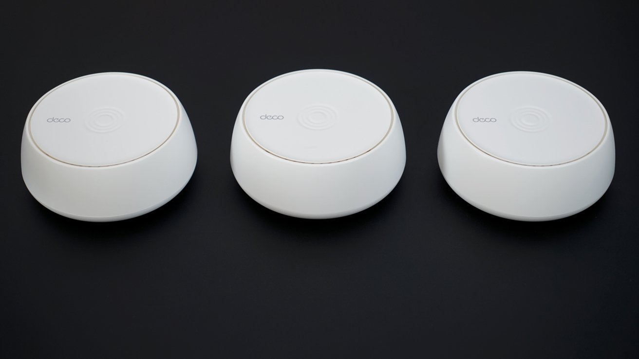 Three white, round electronic devices with subtle branding rest on a black surface, evenly spaced in a row.