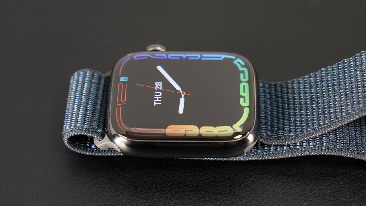 Smartwatch with a colorful display, showing the date 'Thu 28' and time hands over a dark screen, on a textured gray strap.