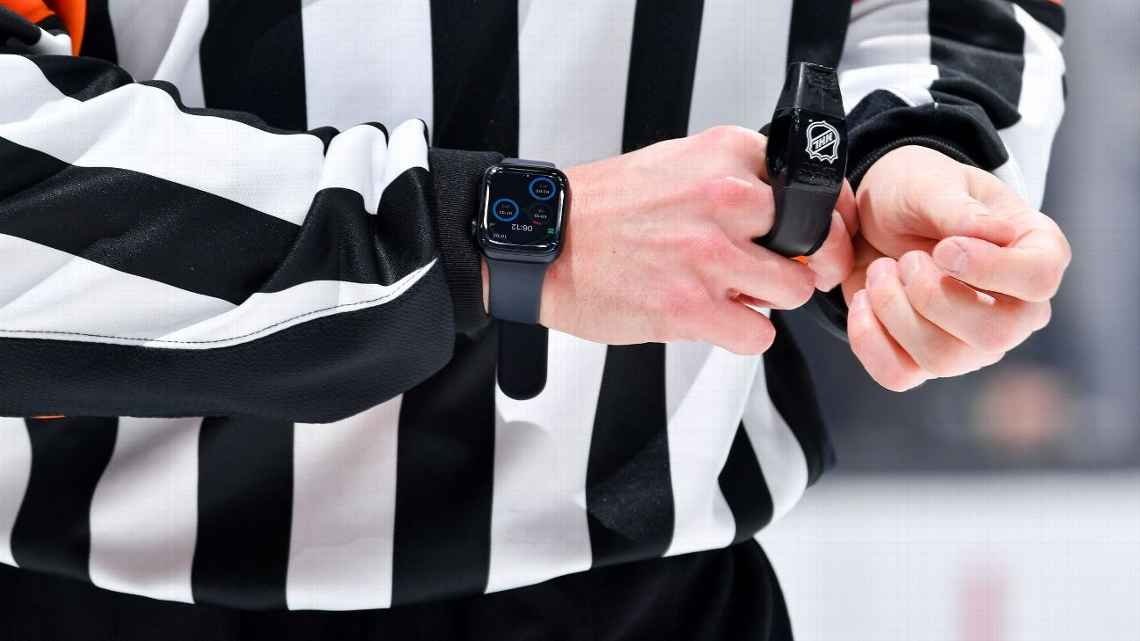 Wasit dalam kaos bergaris hitam dan putih menyesuaikan smartwatch hitam dan perangkat pergelangan tangan dengan logo NHL.