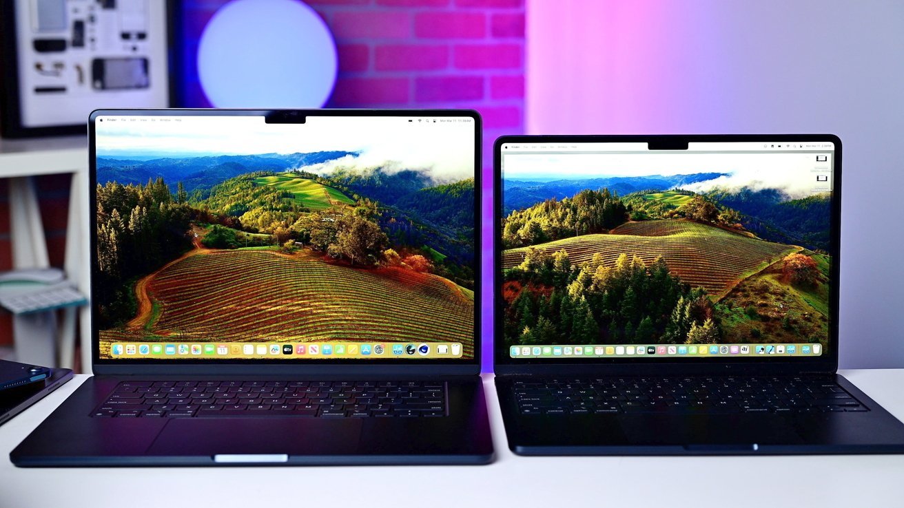 Two laptops side-by-side displaying a vibrant landscape of rolling hills, vineyards, and forests. Background features a blurred room with a glowing light and abstract wall decor.