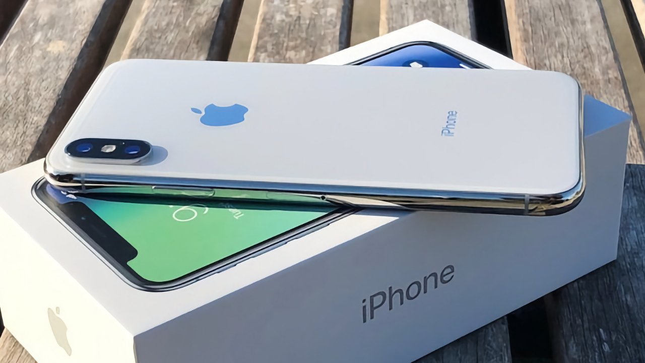 Smartphone placed on its box, featuring dual cameras and an Apple logo, on a wooden surface.