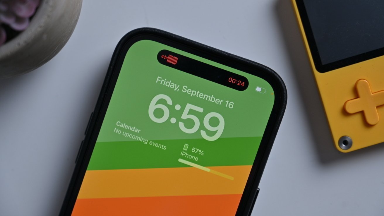 Smartphone screen showing time 6:59, date September 16, green background; nearby is a portable gaming device with a yellow casing and orange cross-shaped button.