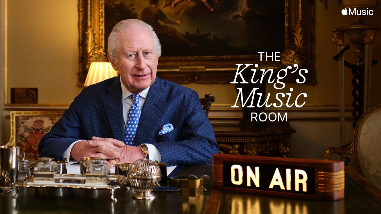 Elderly man in a formal suit sits at a desk in an ornate room with an 'On Air' sign, labeled 'The King's Music Room.'