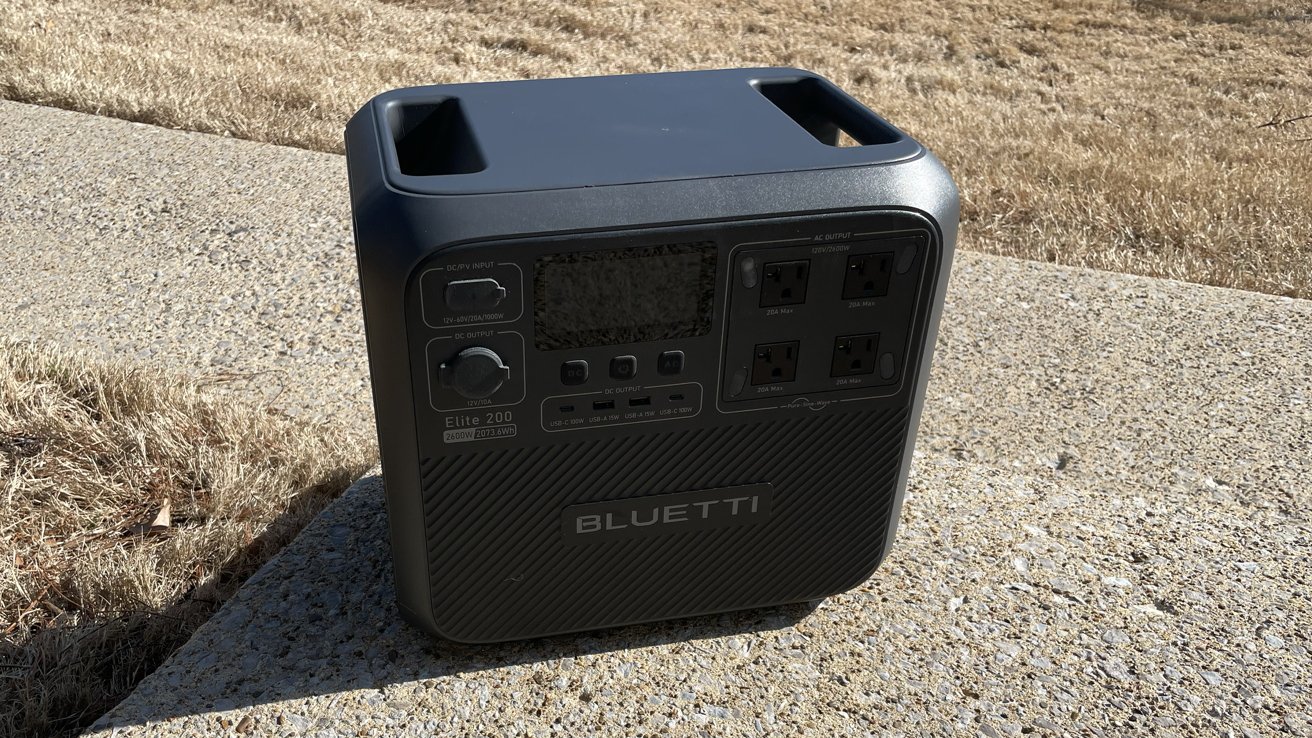 Portable Bluetti power station on a concrete surface, with a grass background, featuring multiple outlets and a digital display.