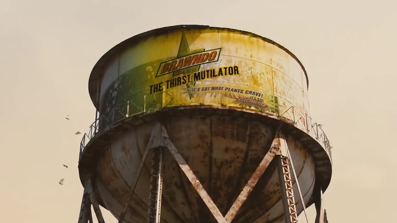 Large rusty water tower with a weathered sign reading Brawndo The Thirst Mutilator against a clear sky background, birds flying nearby.