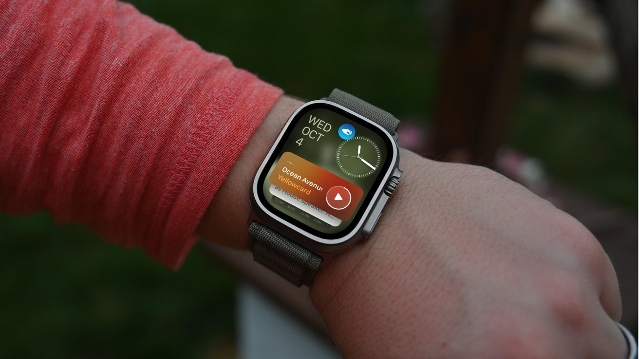 Apple Watch Ultra on wrist displays clock, date, and music player showing 'Ocean Avenue' by Yellowcard. Person is wearing a red sleeve.