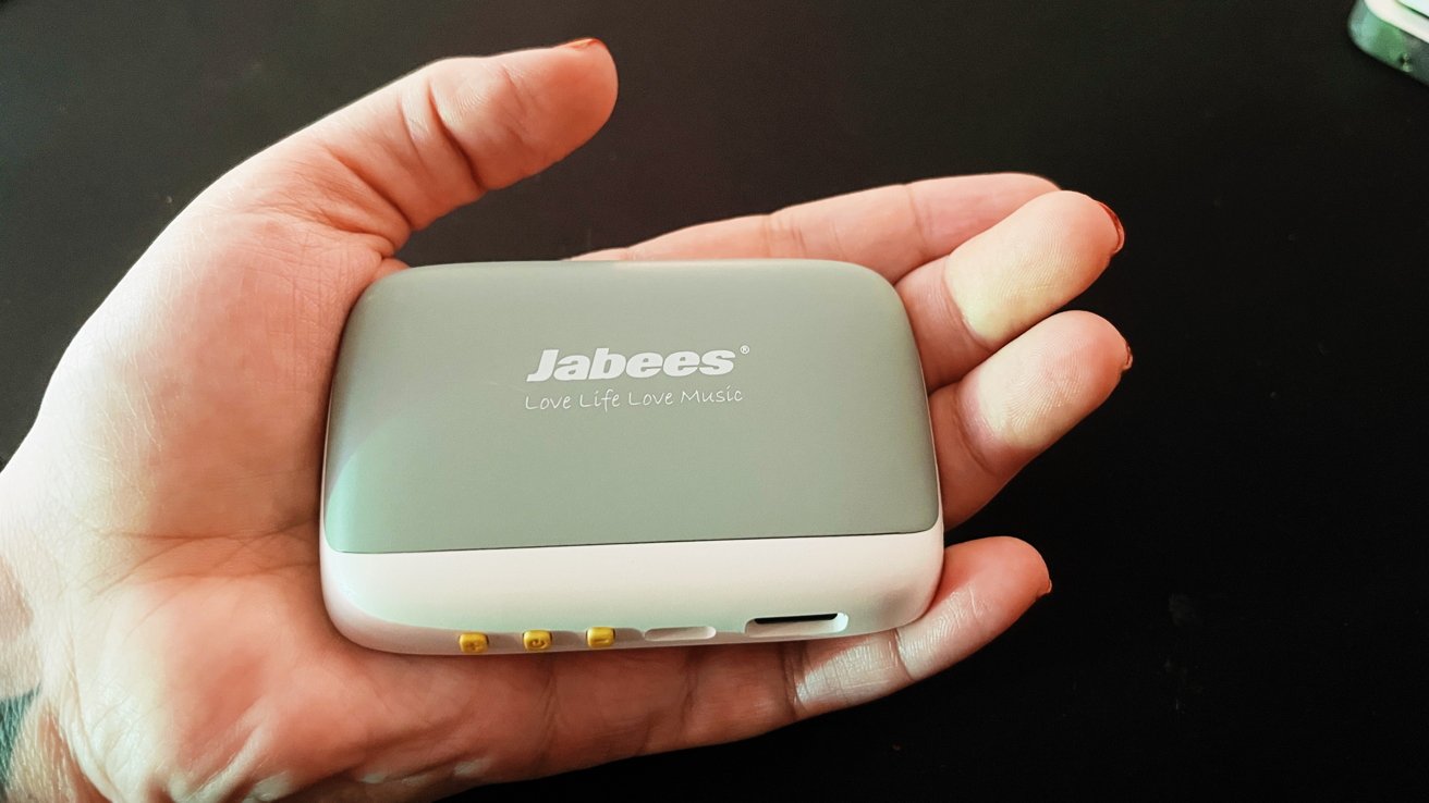 Hand holding a small, gray and white rectangular device with the brand name 'Jabees' and the slogan 'Love Life Love Music' written on it.