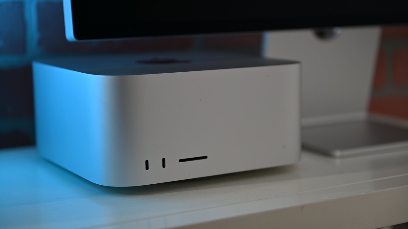 A silver, rectangular computer with rounded edges and ventilation slots, sitting on a white surface, partially lit by blue light.