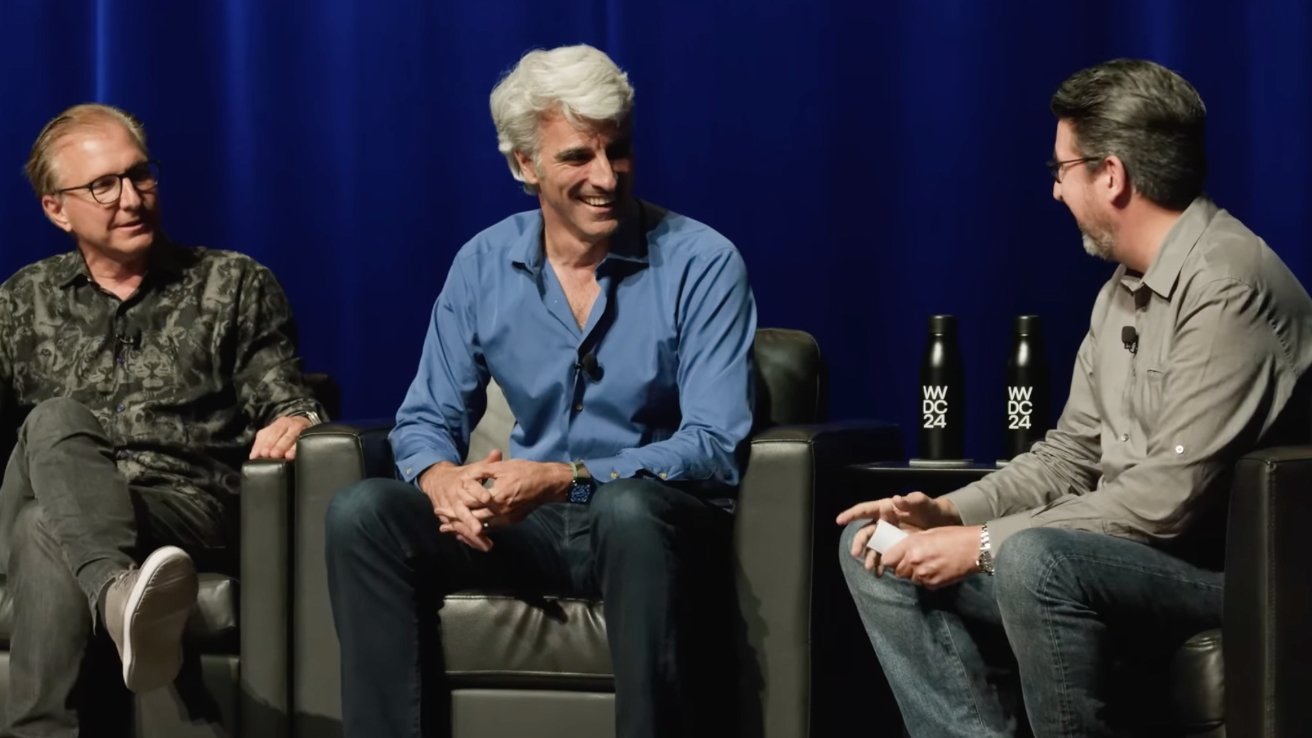 Three men sitting on stage chairs, smiling and talking, with a blue curtain backdrop and event bottles on a table.