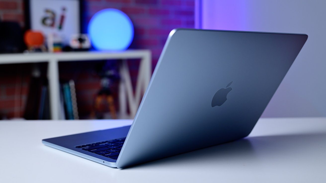 A sleek laptop on a desk with a glowing blue light in the background, positioned on a white shelf with brick wall behind.