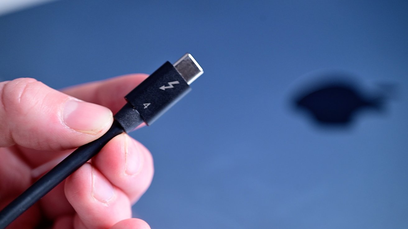 Hand holding a Thunderbolt 4 cable with a close-up of the connector, set against a blurred blue background featuring a logo.