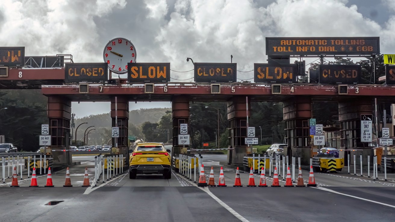 Toll booth with multiple lanes, overhead signs displaying slow or closed, a yellow car approaching, traffic cones, cloudy sky, speed limit signs indicating 25 miles per hour.