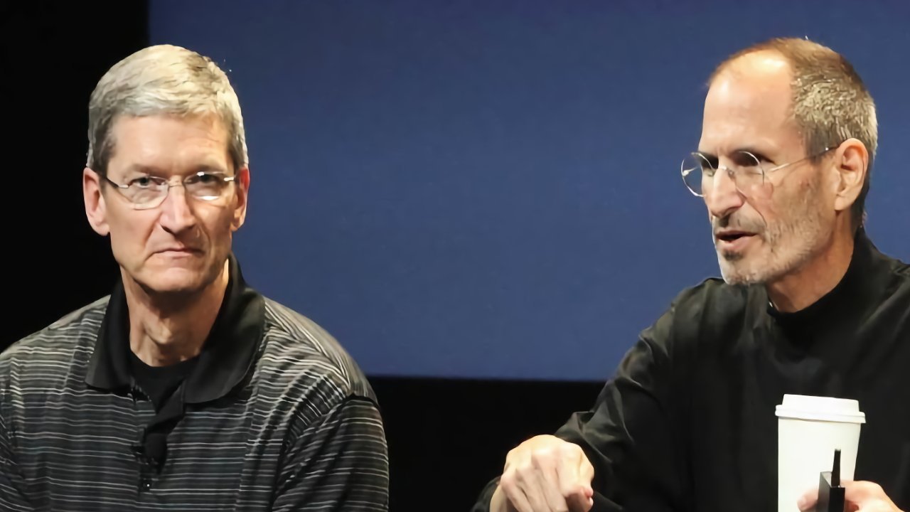 Two men seated, one in glasses and striped shirt, other in black turtleneck holding a white cup, on a blue background.