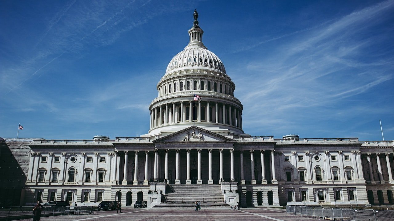 The United States Capitol building with its iconic dome, columns, and American flag, under a clear blue sky.