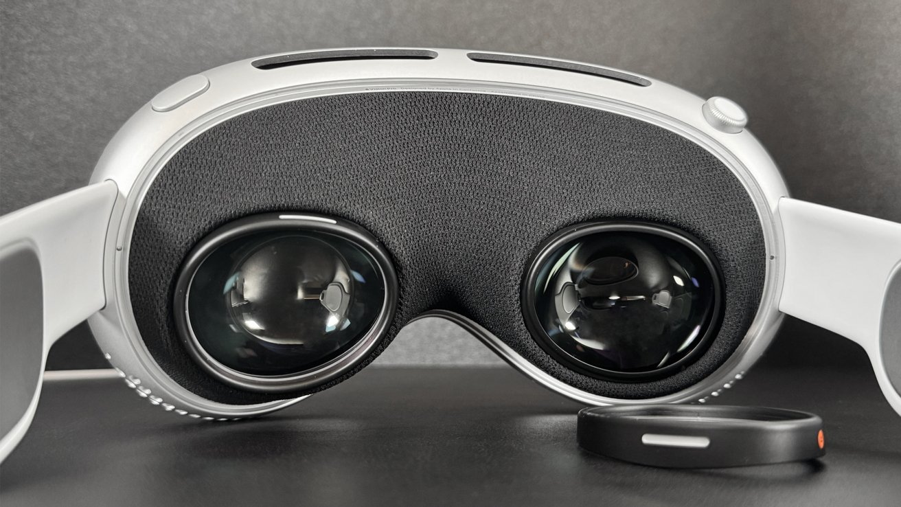 Close-up of a white virtual reality headset with large black lenses and a circular black accessory in front, set against a dark background.