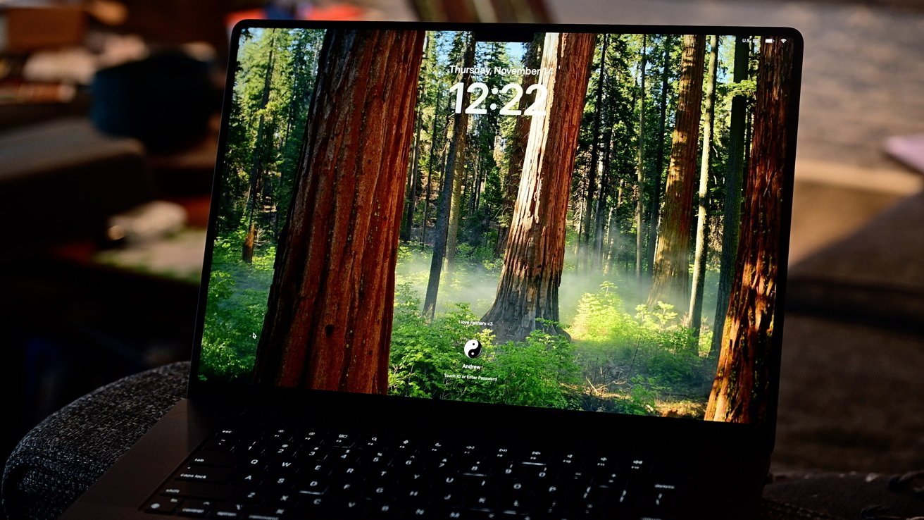 Laptop screen displaying a forest scene with tall trees and sunlit greenery, showing the time 12:22.