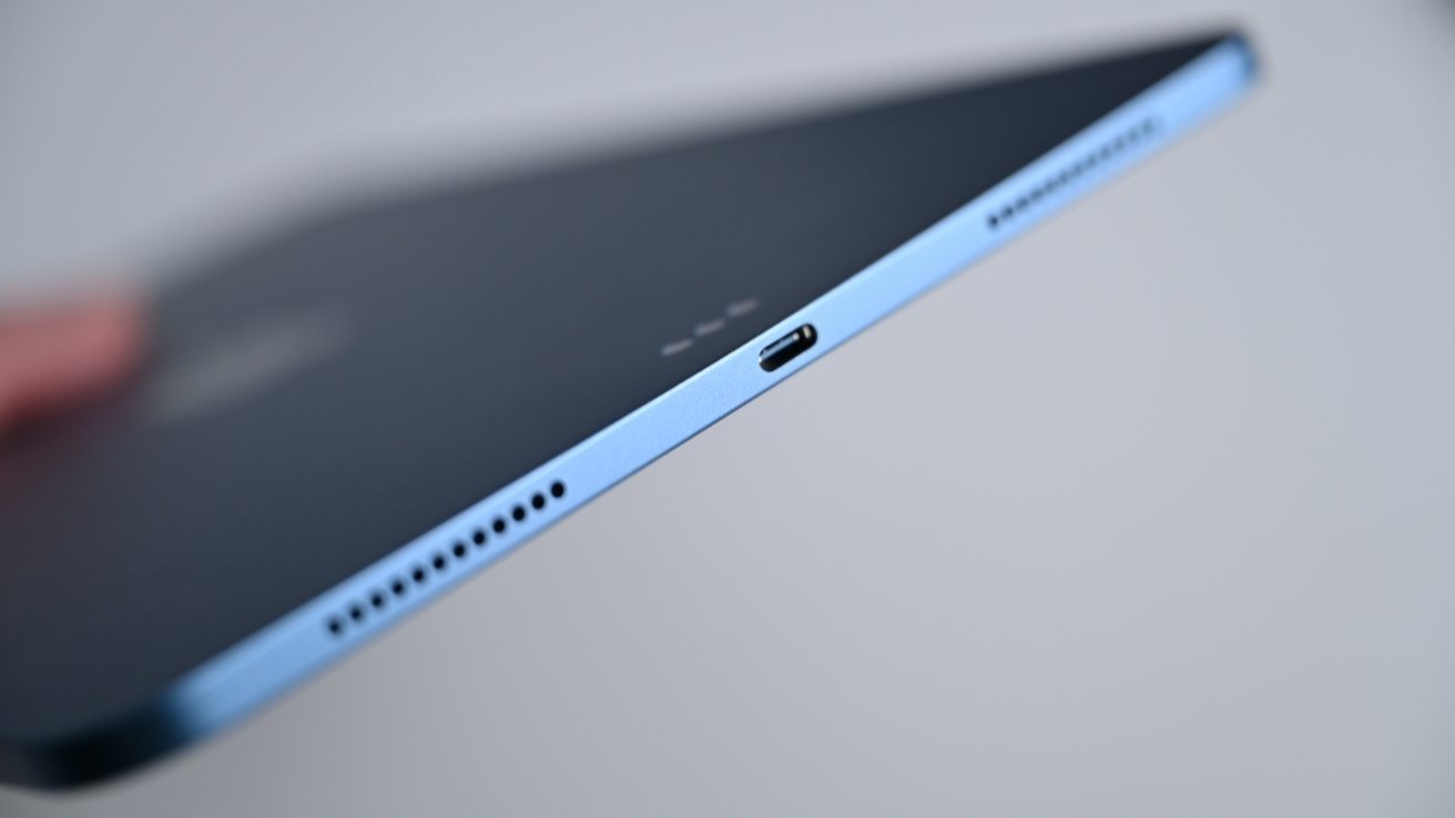 Close-up of a thin electronic device's edge in blue, showing a port and speaker holes.