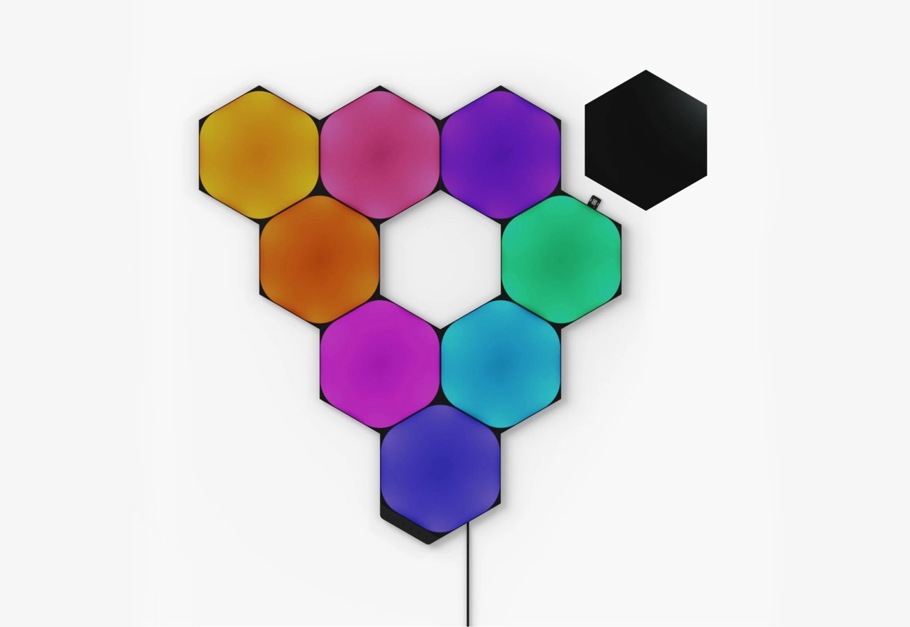 Hexagonal light panels arranged in a bee-hive pattern, displaying vibrant colors such as yellow, pink, orange, purple, and blue on a white background, with one black panel detached.