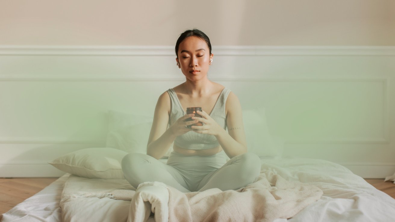 A person sits cross-legged on a bed, eyes closed, holding a small jar, in a calm, softly lit room.