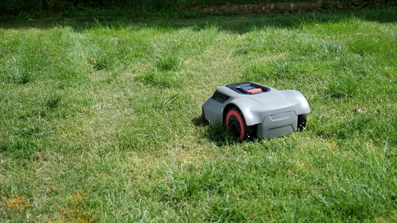 Robotic lawn mower on grass, surrounded by a lush green lawn, under bright sunlight.