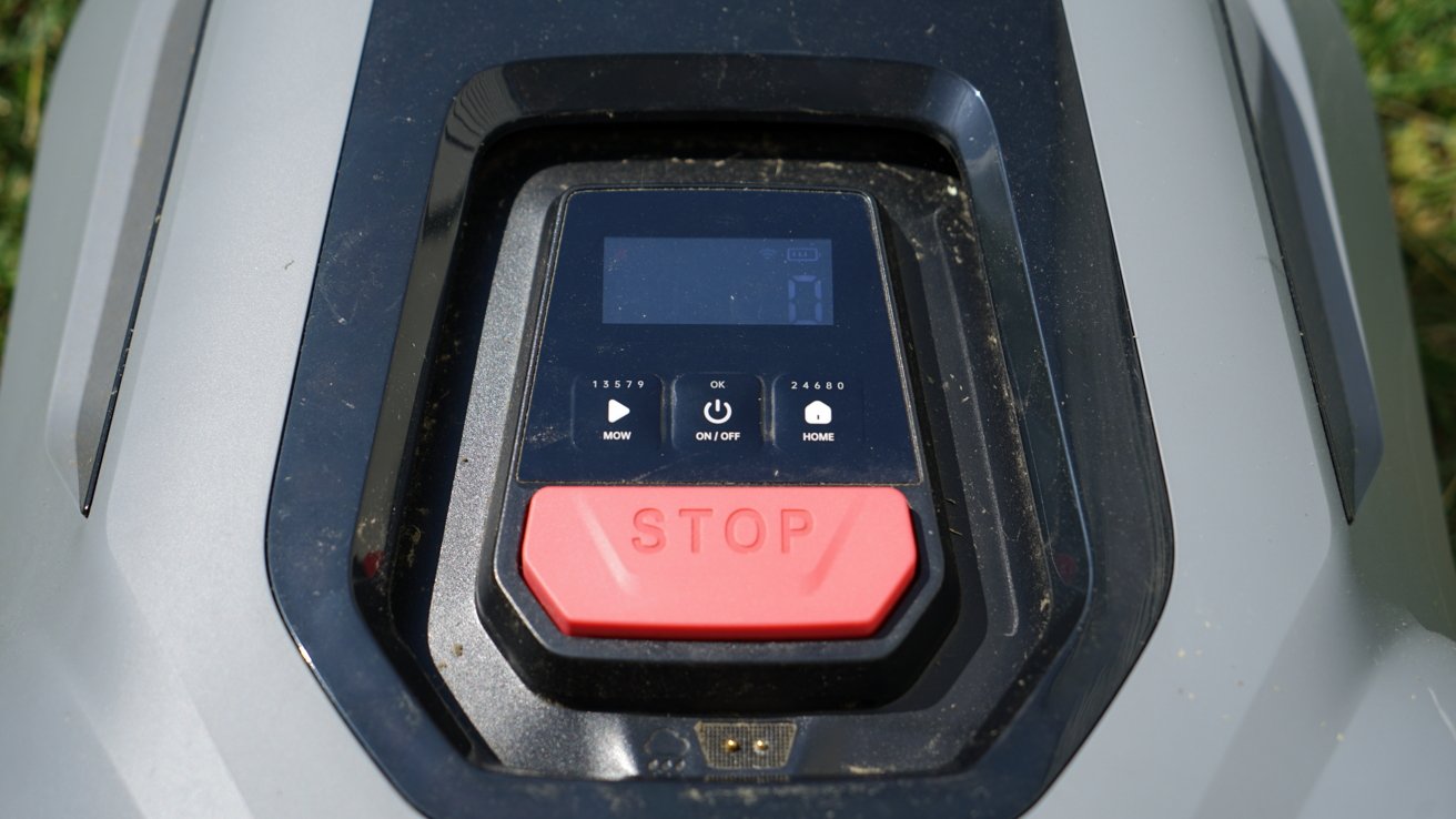 Close-up of a control panel featuring a large red stop button, small display screen, and various function buttons on a lawn mower.