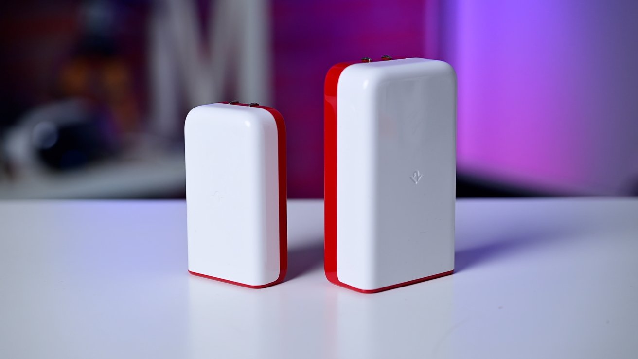 Two white, rectangular devices with red edges, standing upright on a white surface, against a blurred, purple background.
