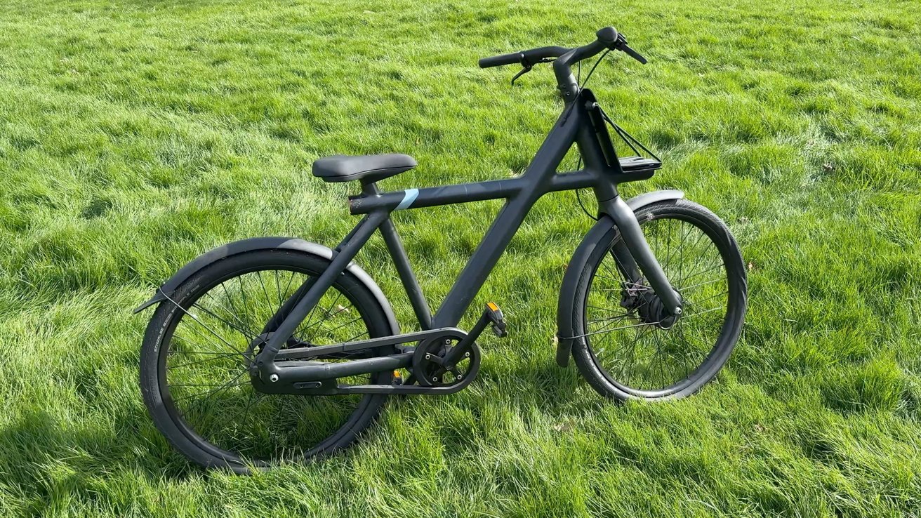 Black bicycle on lush green grass, featuring a sleek frame, straight handlebars, and disc brakes, with a comfortable seat and fenders on both wheels.