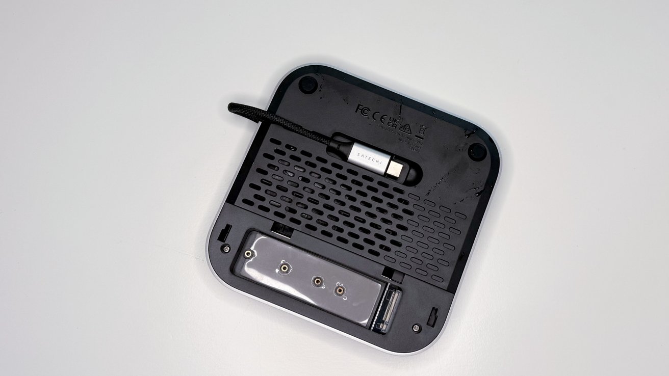 Square electronic device underside with ventilation holes, a tucked cable labeled 'Satechi,' and various connectors on a white surface.