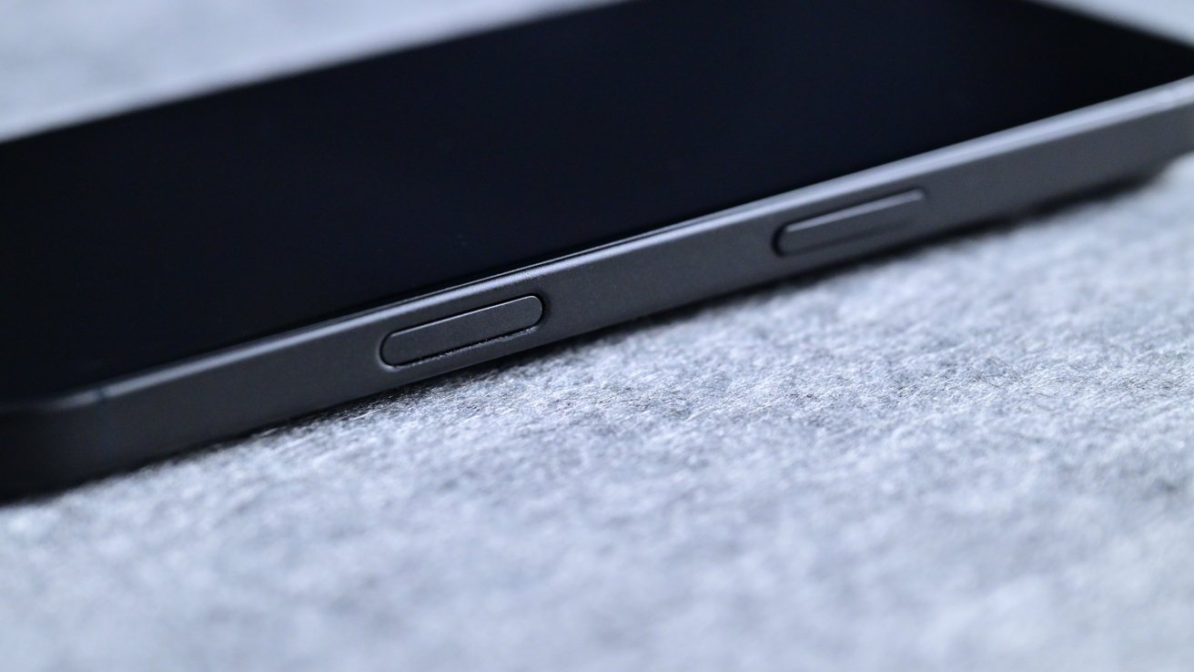 Close-up of a black smartphone laying on a soft gray surface, focusing on side buttons.