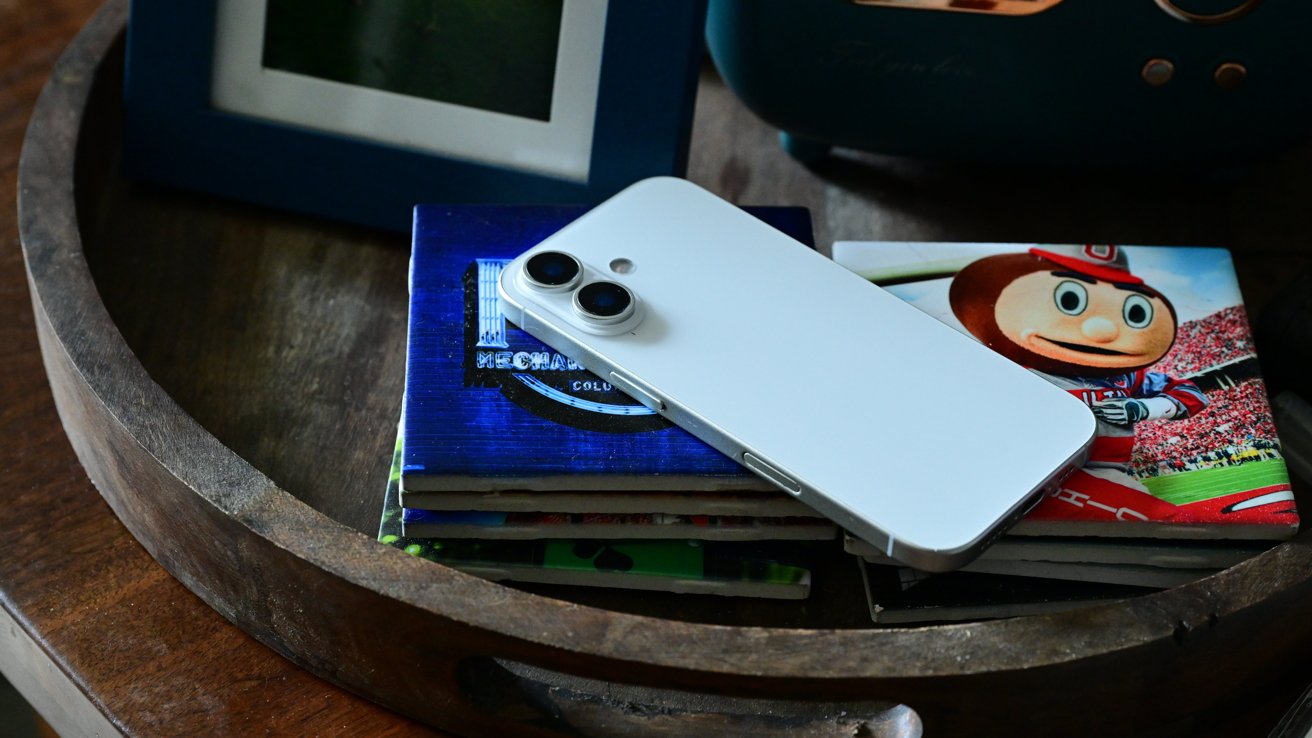 White smartphone with dual cameras on coasters featuring a cartoon character and various designs, in a round wooden tray on a wooden surface.