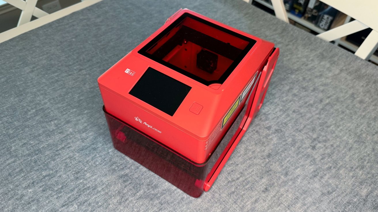 Red desktop 3D printer on a gray surface with a transparent cover and small control panel on top.