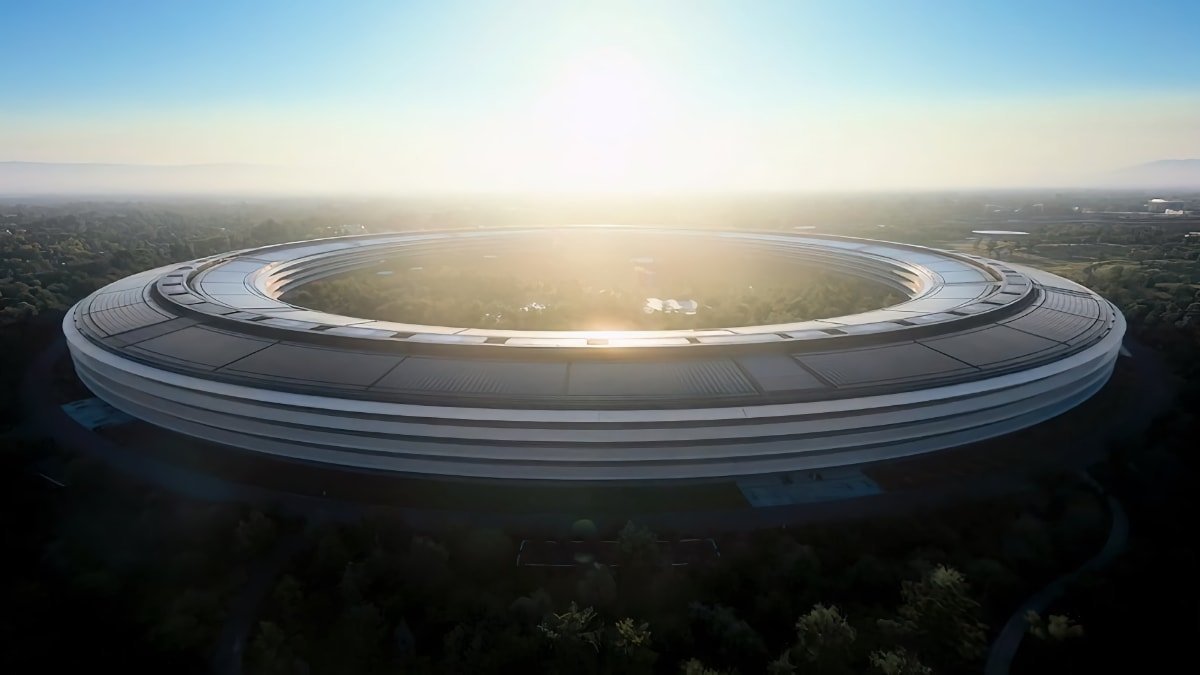 Aerial view of a large, circular building surrounded by trees at sunrise, with sunlight reflecting off the structure.