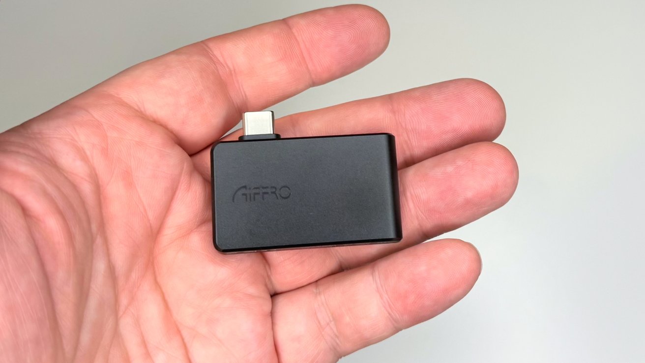 A hand holds a small black rectangular device with a USB-C connector on one side.