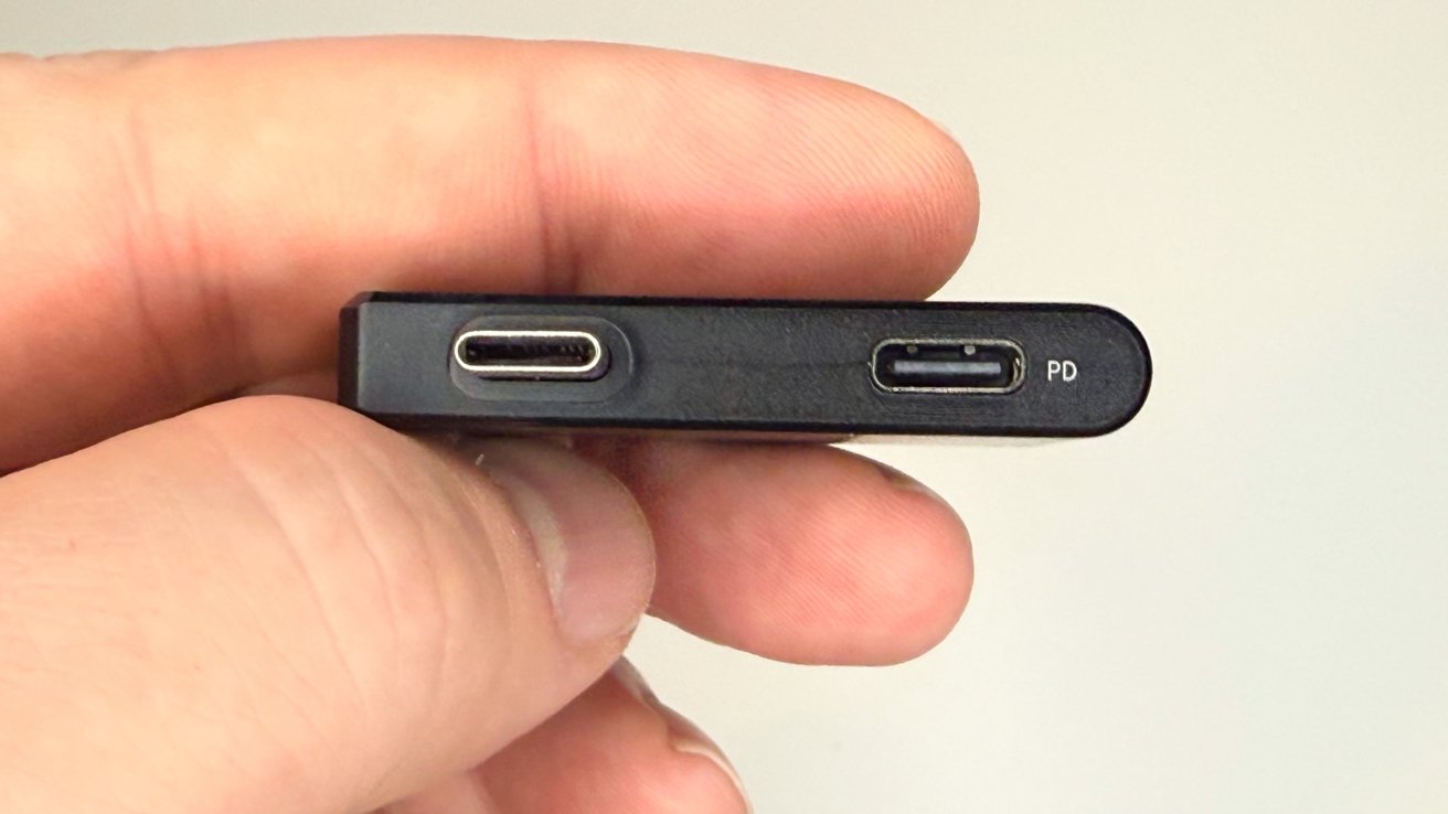 A hand holds a small black electronic device with two ports: one USB-C and one marked 'PD'.