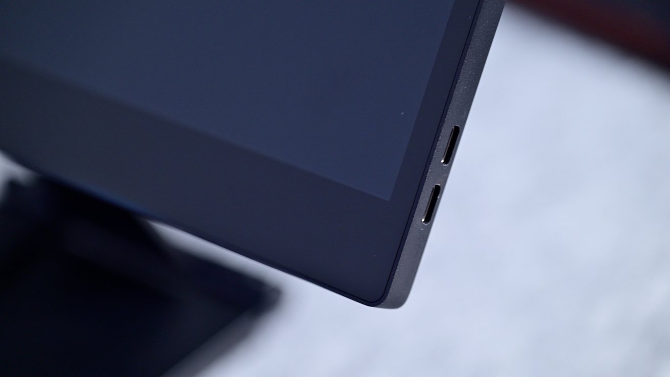 Close-up of a black computer monitor corner featuring two USB-C ports against a blurred gray background.