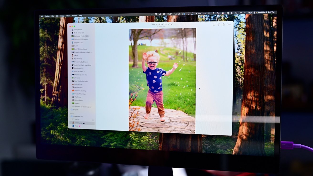A computer screen displays a photo of a joyful child with glasses running on a pathway, surrounded by bubbles and greenery.