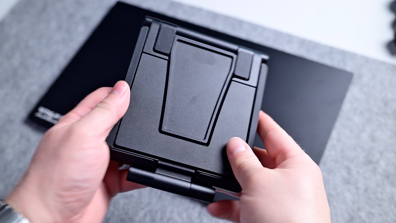 Hands holding a folded black VR headset with a geometric design, against a gray and black background.