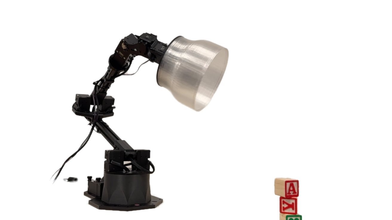 Robotic arm with a large, conical light fixture reaches towards three stacked alphabet blocks on a white background.