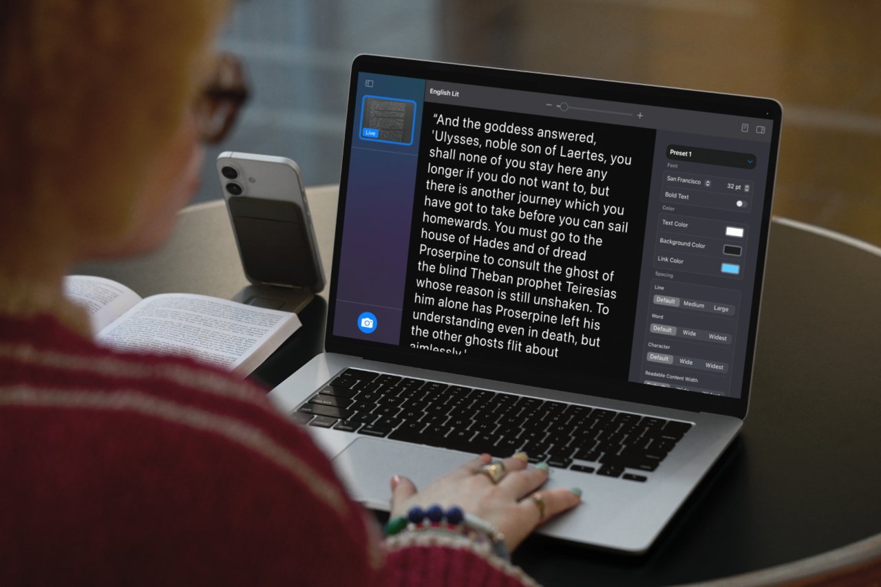 Person reading from an open book and laptop with text editor, large font displaying text and formatting options visible on screen, smartphone nearby.