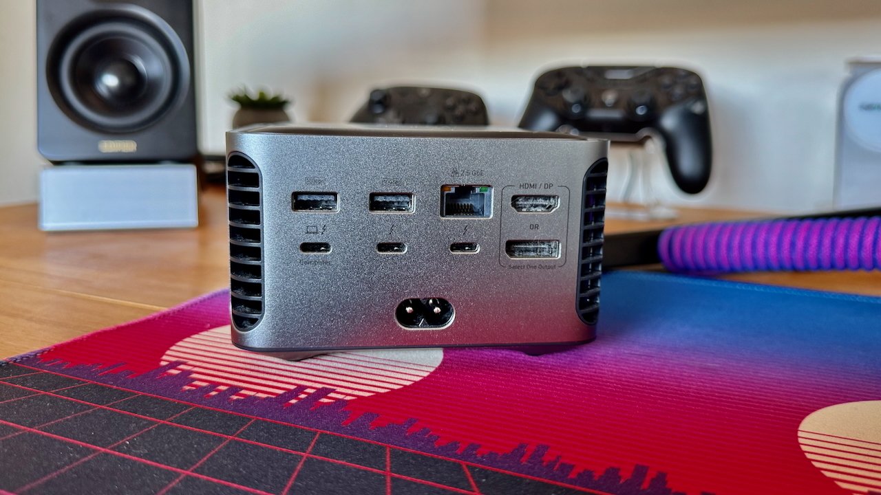 Anker dock from the rear, showing ports, on a desk, surrounded by colorful mat, speakers, and gaming controllers in the background.