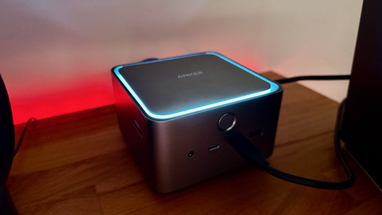 Anker dock with glowing blue outline on top, placed on a wooden surface. It has multiple ports and is connected by a black cable.