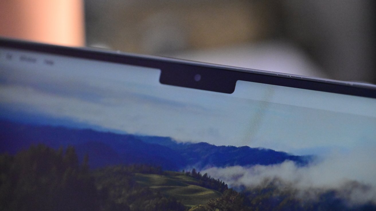 Close-up of a laptop screen showing a landscape wallpaper with hills and clouds, featuring a notch at the top center.