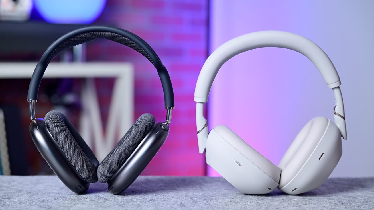 Two pairs of over-ear headphones on a table, one black with dark ear cushions, the other white with light ear cushions, against a blurred purple background.