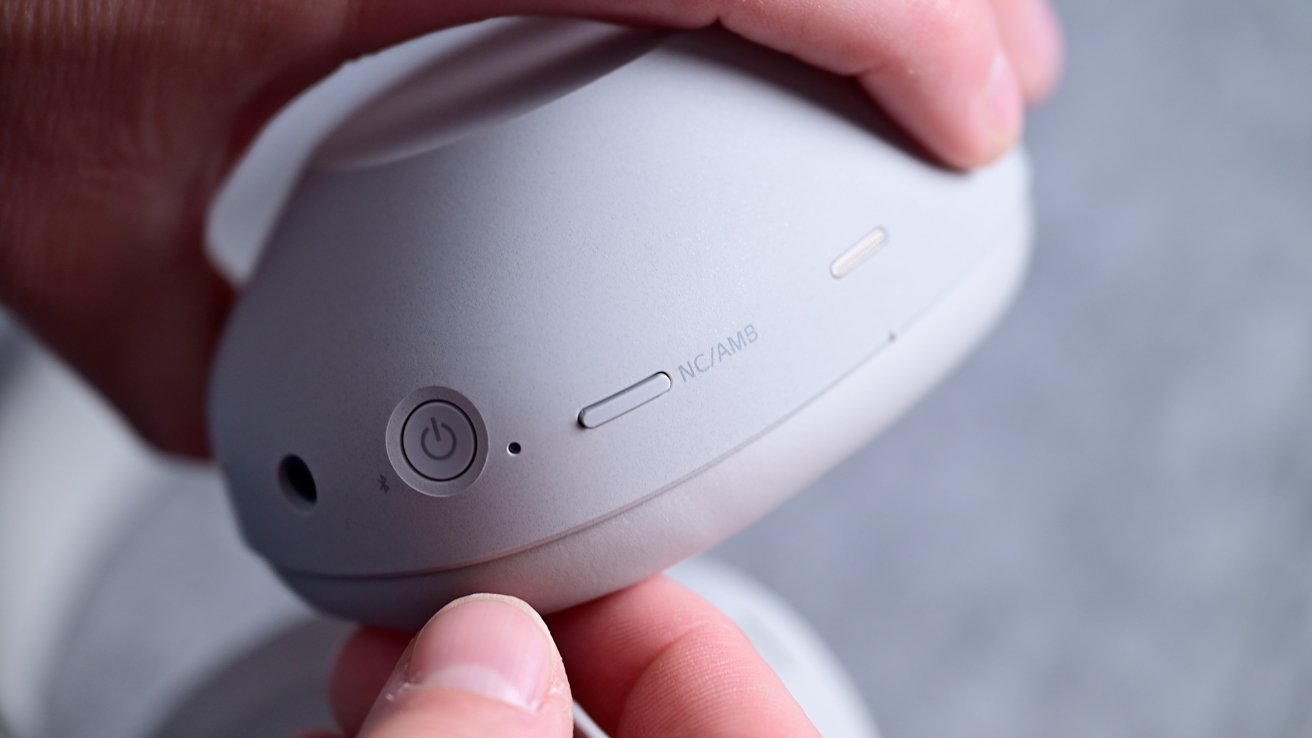 Person holding a gray headphone cup focusing on power button and controls labeled NC/AMB.