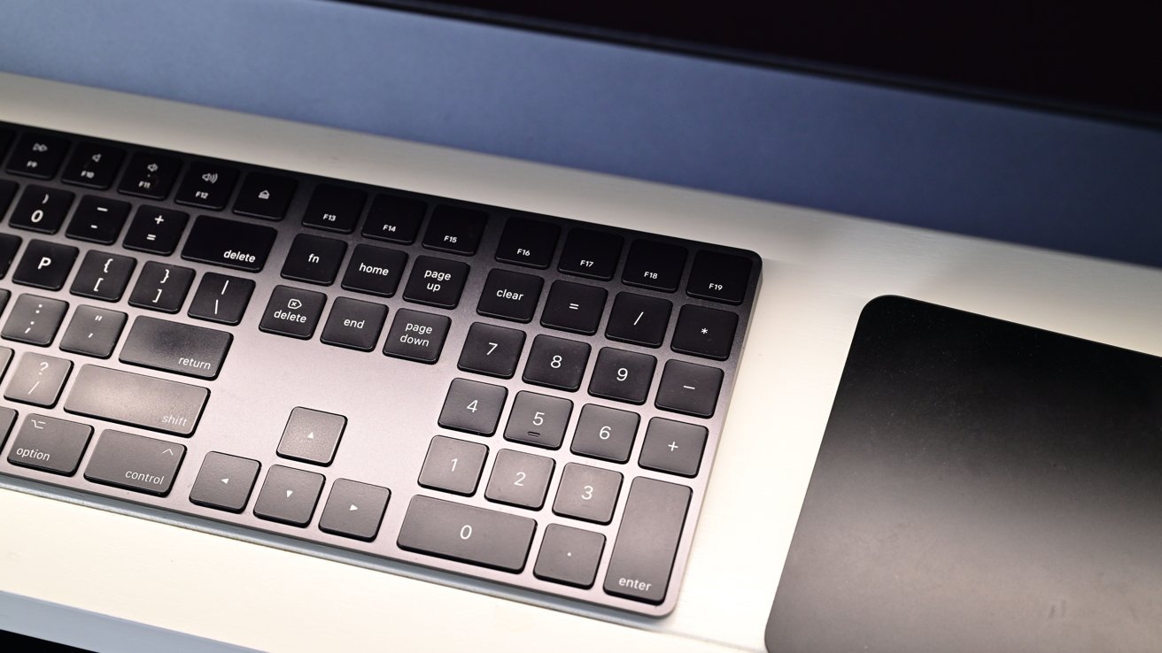Black computer keyboard with numeric keypad next to a black trackpad on a white desktop.