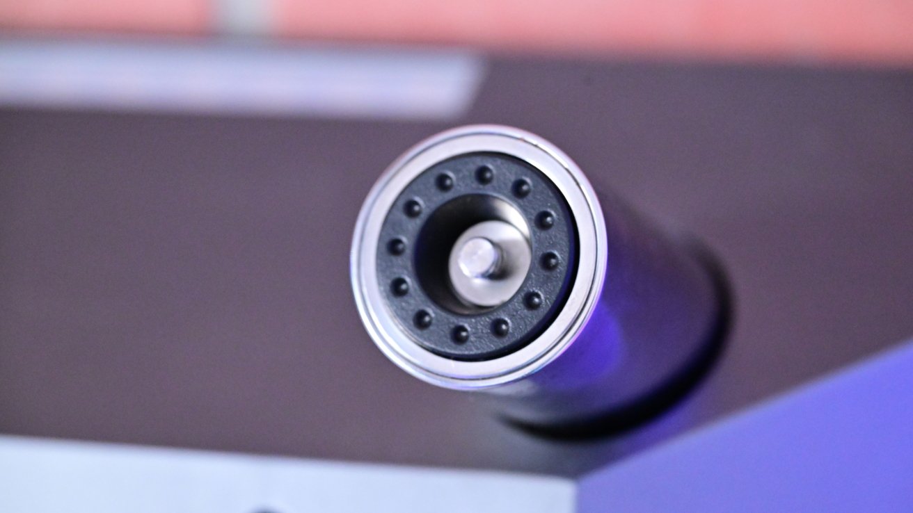 Close-up of a microphone's circular top with a metal grille and small round openings, mounted on a cylindrical body.